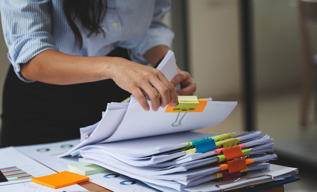 Businesswoman hands working in Stacks of paper files for searching and checking unfinished document achieves on folders papers